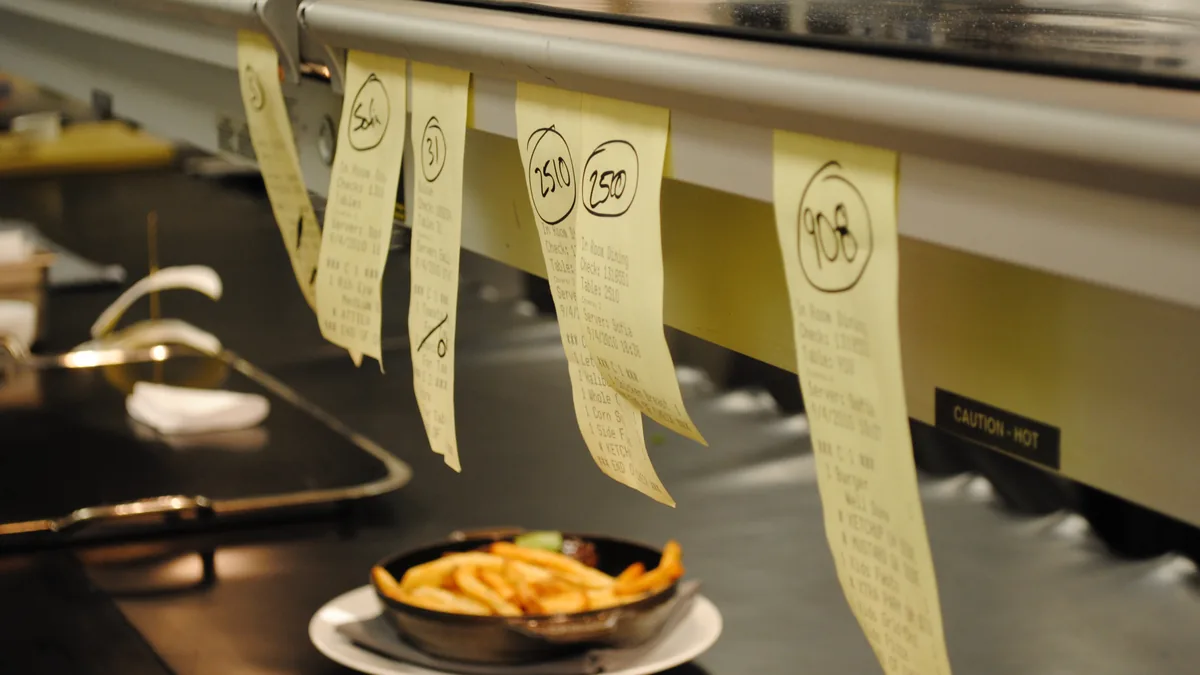 Order tickets hanging on the rail above the pass, a dish of fries waiting below.