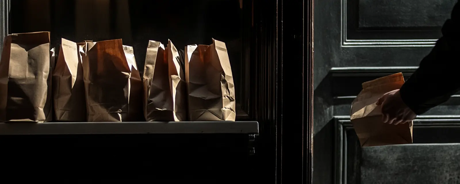 Bagged orders on a shelf by the door, a hand taking one.